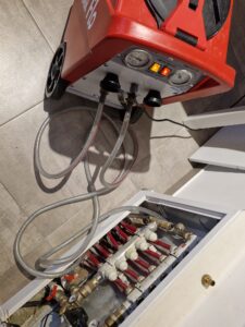 Mașină de curățare profesională a sistemelor de încălzire în pardoseală, conectată la un distribuitor de circuite de încălzire, utilizată pentru eliminarea depunerilor și a eficientizării sistemului termic.